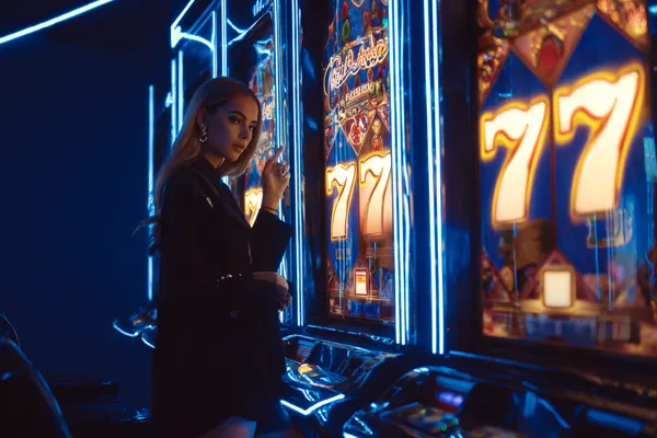 A woman smiling by bright slot machines showing lucky symbols, showcasing the exciting slot offerings at SPORTYBEF.